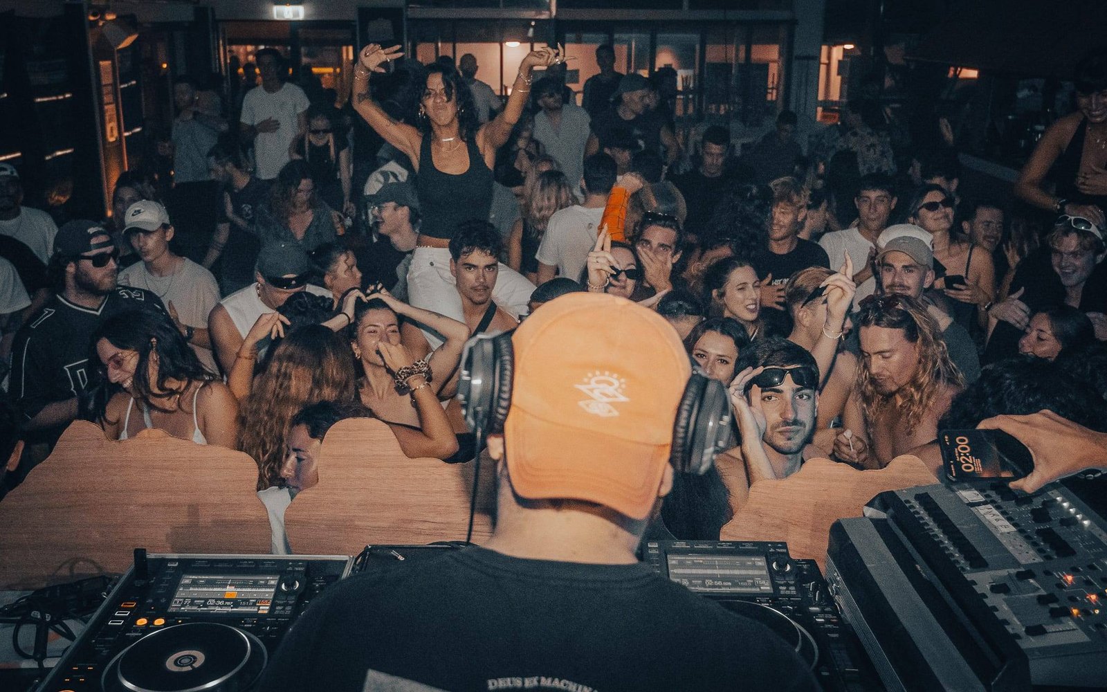 A DJ in an orange cap playing to a packed club room
