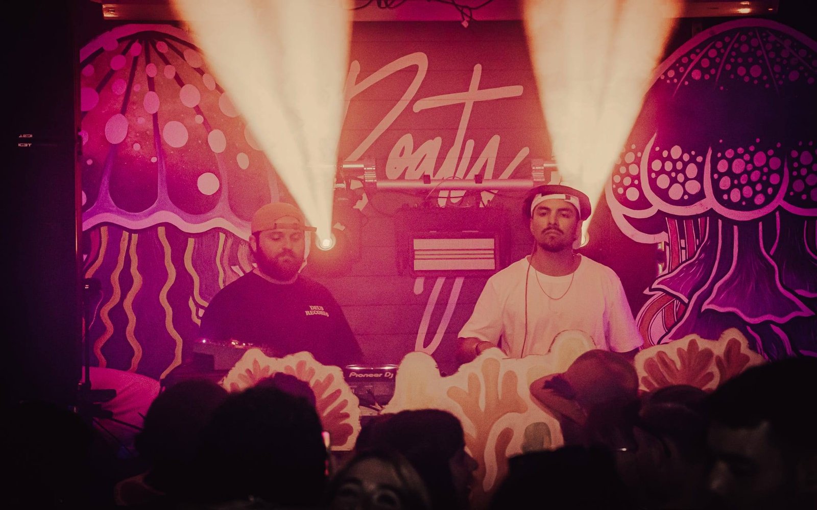 Two DJs under spotlights in front of a jellyfish mural
