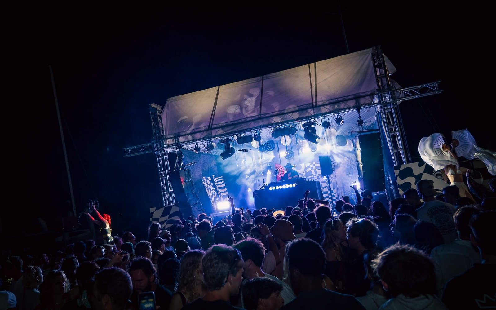 A packed crowd in front of an open-air BLOOM stage lit in blue at night