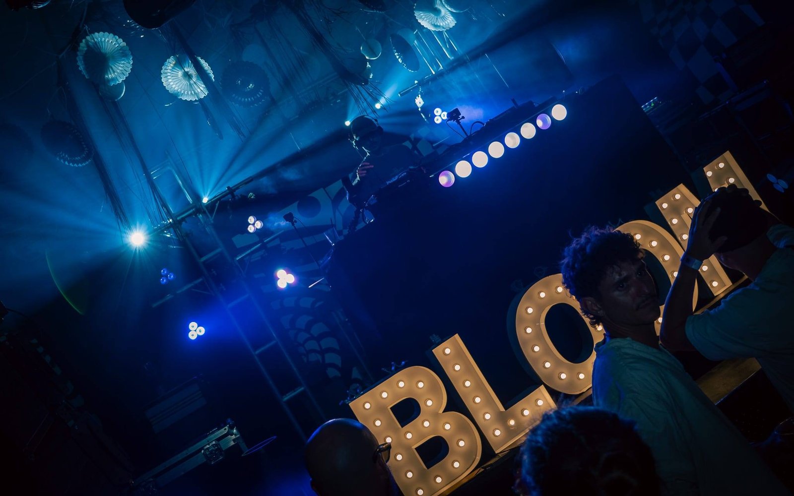 Stage lights cutting through haze above glowing BLOOM marquee letters